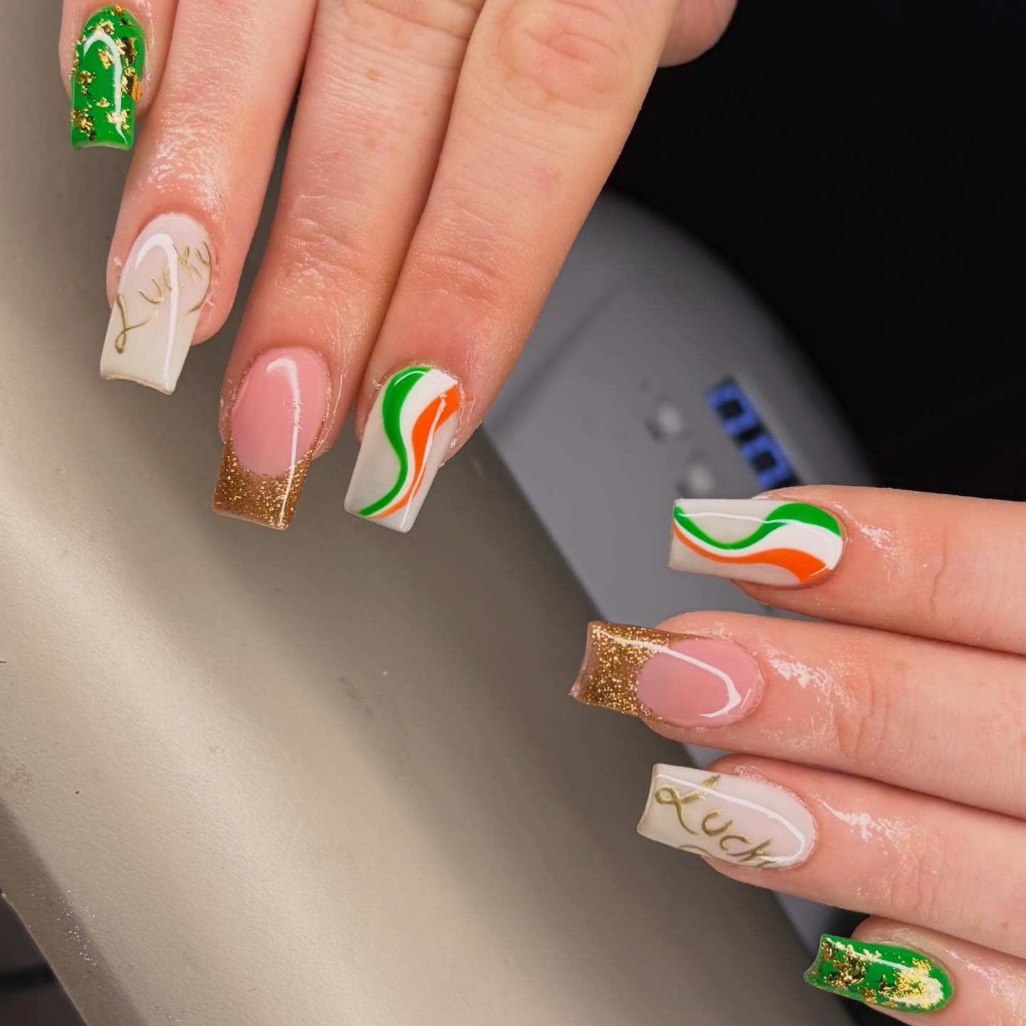 St. Patrick's themed square nails with gold glitter french tips, green and orange swirls and gold Lucky lettering