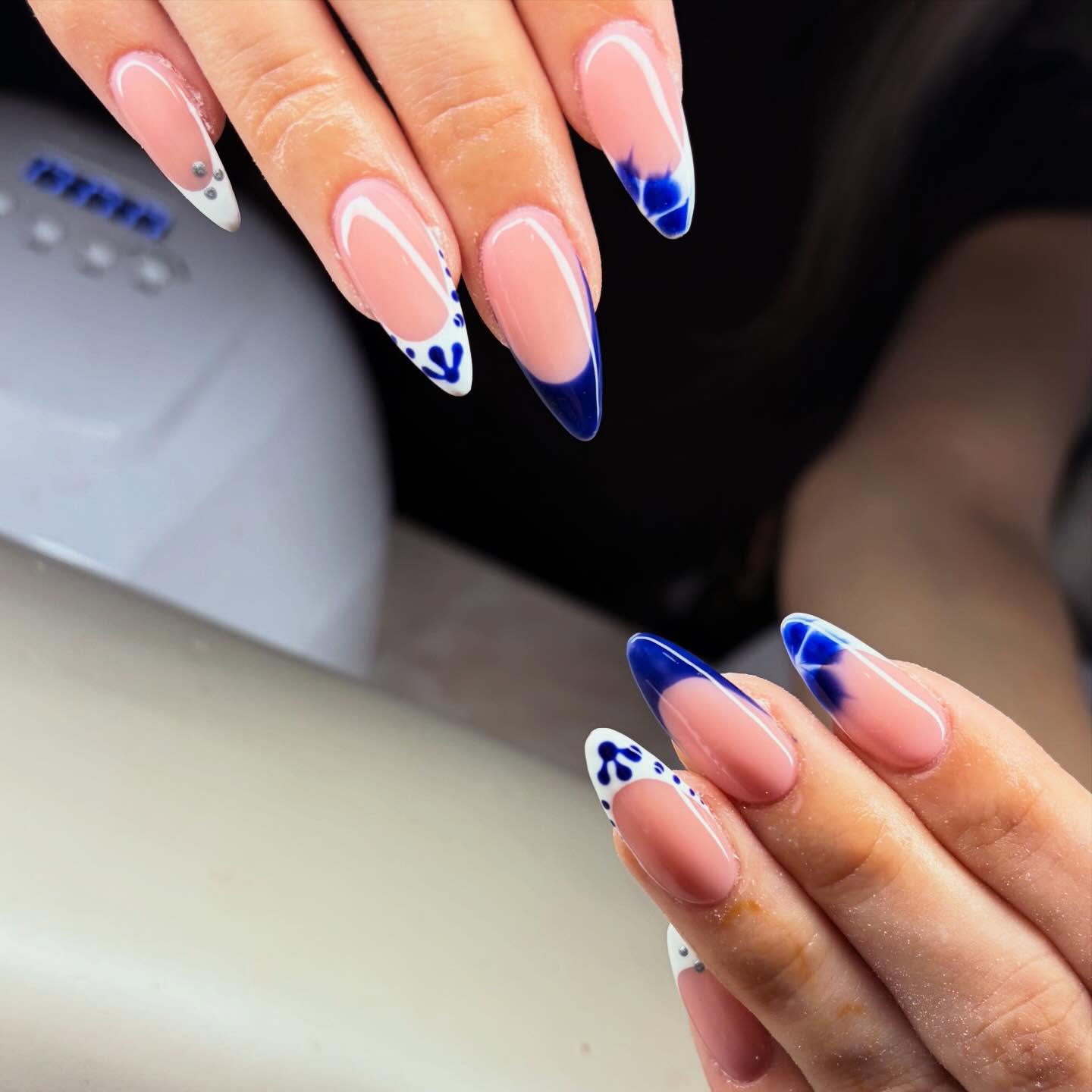 Classic nude almond nails with royal blue porcelain-inspired french tips and delicate ink flourishes