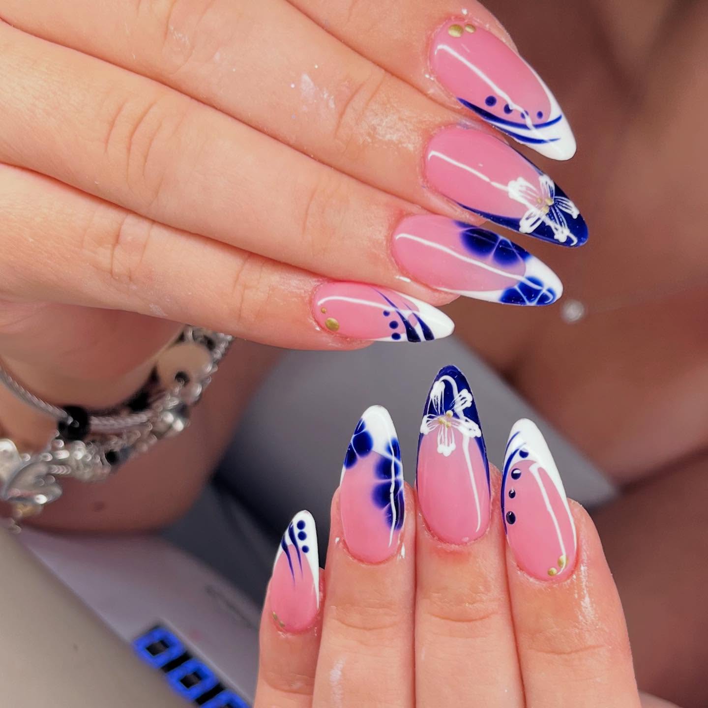 Vibrant pink almond nails with blue watercolor marble tips and hand-painted white floral details